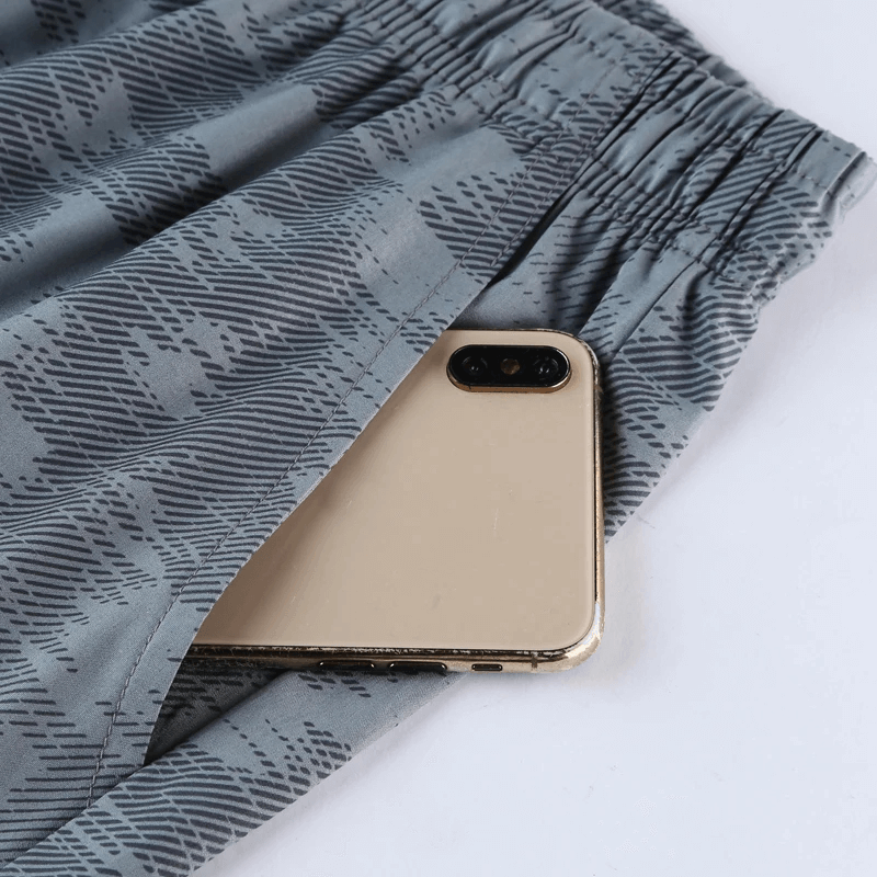 Camouflage athletic shorts with side pocket holding a smartphone, featuring quick-dry fabric and elastic waistband. Perfect for workouts.
